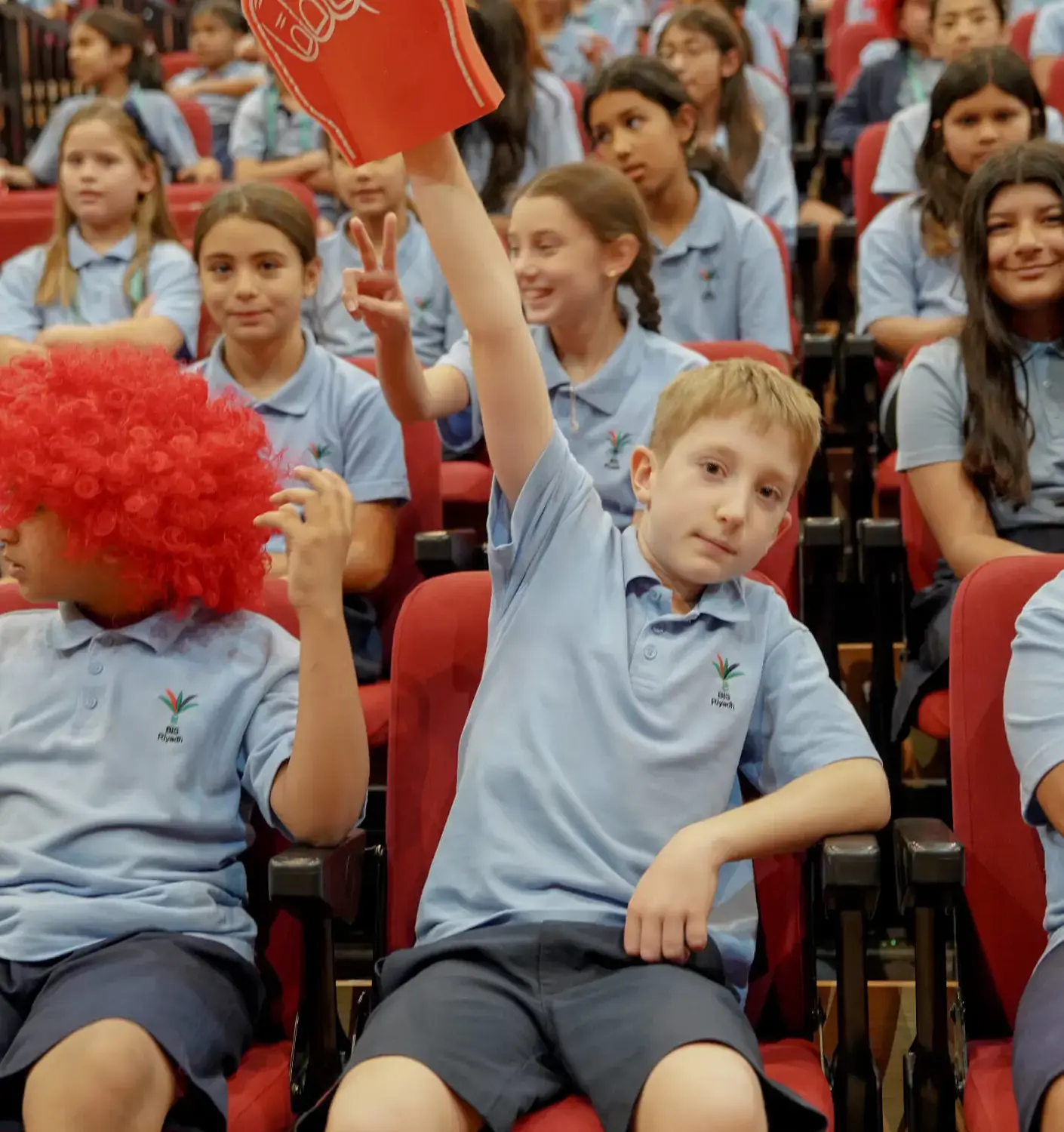 BISR Al Hamra students cheering and waving foam fingers at a school event.