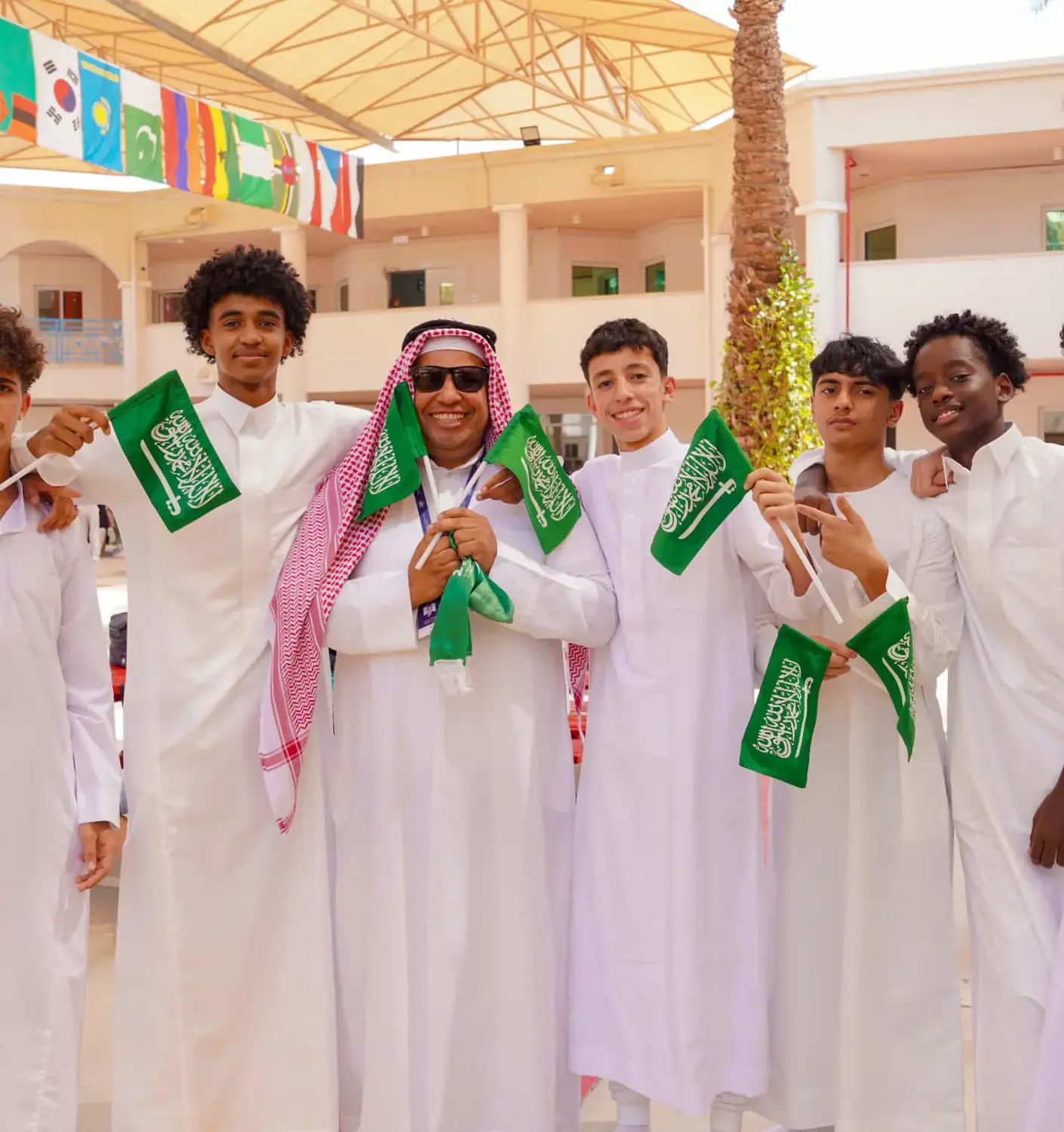 BISR Al Hamra students and teacher smile while holding Saudi flags.
